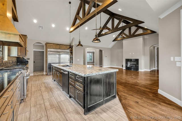 3805 S Tamarack Ave, Broken Arrow, OK 74011 - kitchen with arched walkways, appliances with stainless steel finishes, premium range hood, high vaulted ceiling, and a large island with sink