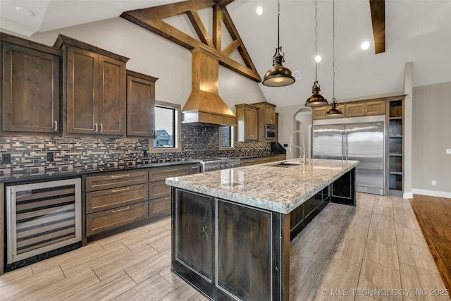 3805 S Tamarack Ave, Broken Arrow, OK 74011 - kitchen featuring beverage cooler, appliances with stainless steel finishes, a sink, custom range hood, and a center island with sink