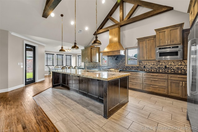 3805 S Tamarack Ave, Broken Arrow, OK 74011 - kitchen featuring an island with sink, light wood-style flooring, high vaulted ceiling, backsplash, and light stone counters