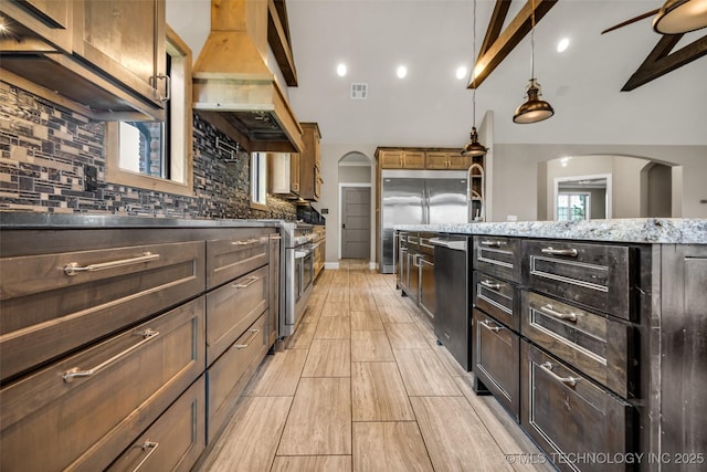 3805 S Tamarack Ave, Broken Arrow, OK 74011 - kitchen featuring premium appliances, custom range hood, backsplash, arched walkways, and light stone countertops