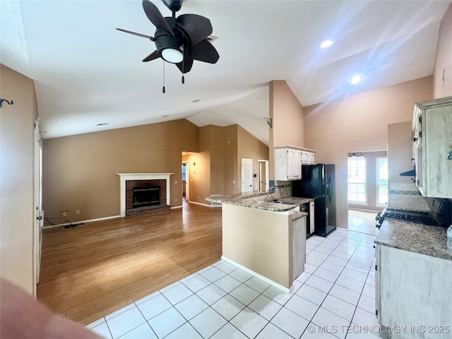915 Aspenwood St, Cleveland, OK 74020 - kitchen featuring freestanding refrigerator, a brick fireplace, a peninsula, vaulted ceiling, and light tile patterned flooring