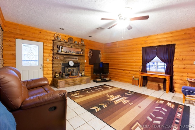 200 S K St, Quinton, OK 74561 - living room featuring a wood stove, light tile patterned flooring, rustic walls, ceiling fan, and a textured ceiling