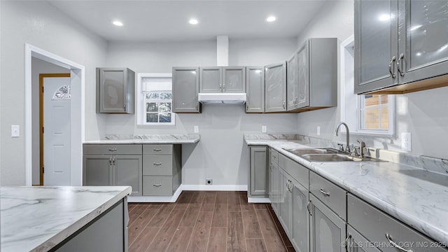 613 NW A St, Ardmore, OK 73401 - kitchen featuring gray cabinets, a sink, dark wood-style floors, under cabinet range hood, and light stone countertops