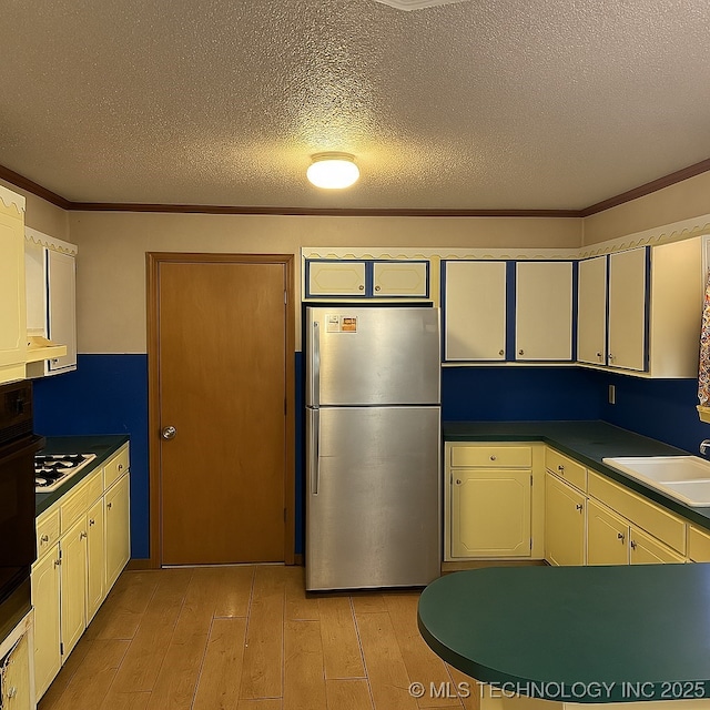 205 N Ash St, Bristow, OK 74010 - kitchen featuring freestanding refrigerator, a sink, light wood-style flooring, ornamental molding, and a textured ceiling