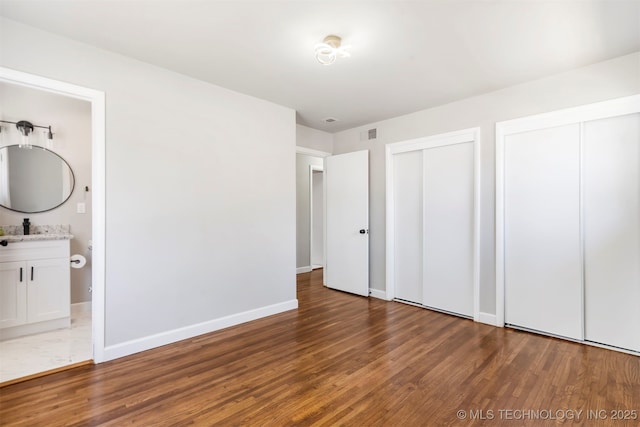 5939 E 26th St, Tulsa, OK 74114 - unfurnished bedroom featuring two closets, wood finished floors, baseboards, and connected bathroom