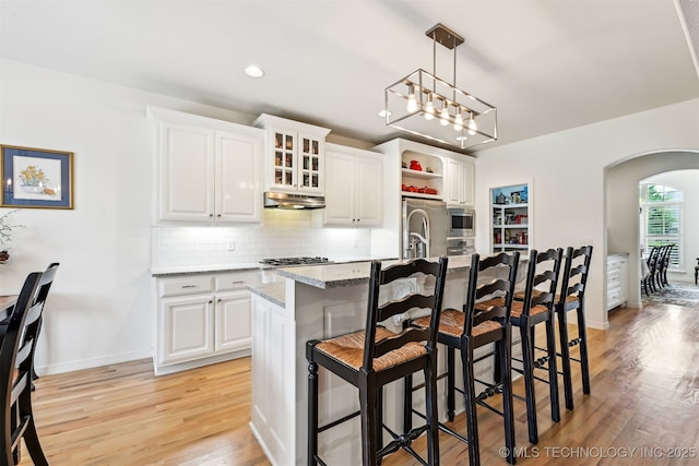 16425 E 49th St, Tulsa, OK 74134 - kitchen with arched walkways, light wood-style flooring, decorative backsplash, a breakfast bar area, and white cabinets