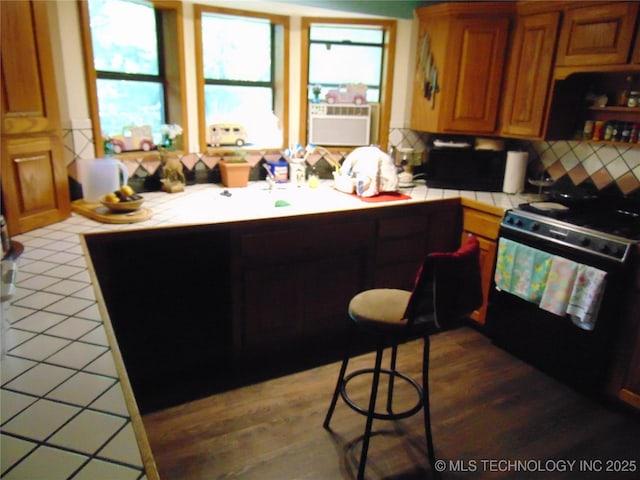 6721 Swayback, Sulphur, OK 73086 - kitchen featuring range with gas cooktop, tile counters, decorative backsplash, wood finished floors, and brown cabinets