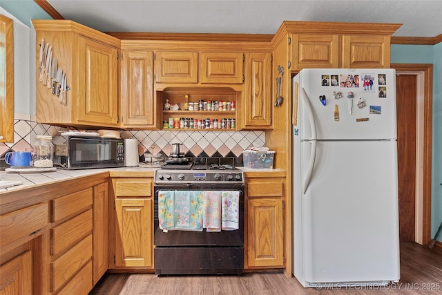 6721 Swayback, Sulphur, OK 73086 - kitchen with freestanding refrigerator, gas range oven, tile counters, black microwave, and tasteful backsplash