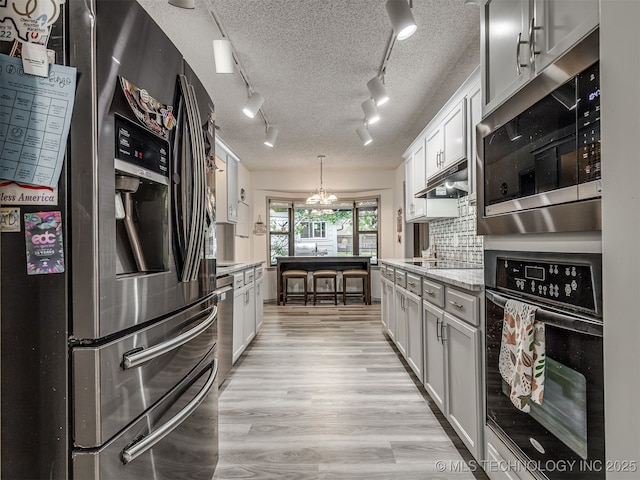 25206 E 64th St, Broken Arrow, OK 74012 - kitchen featuring appliances with stainless steel finishes, light wood-type flooring, a chandelier, rail lighting, and decorative backsplash