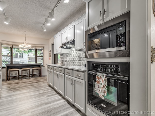 25206 E 64th St, Broken Arrow, OK 74012 - kitchen with black oven, built in microwave, rail lighting, backsplash, and under cabinet range hood