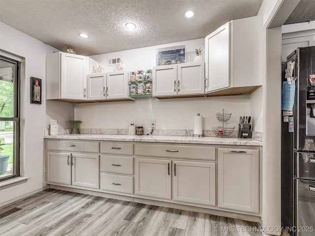 25206 E 64th St, Broken Arrow, OK 74012 - kitchen featuring black fridge with ice dispenser, a textured ceiling, light wood finished floors, recessed lighting, and light stone counters