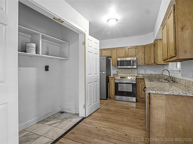 148 W 4th, Atoka, OK 74525 - kitchen featuring appliances with stainless steel finishes, a sink, brown cabinetry, light stone counters, and baseboards