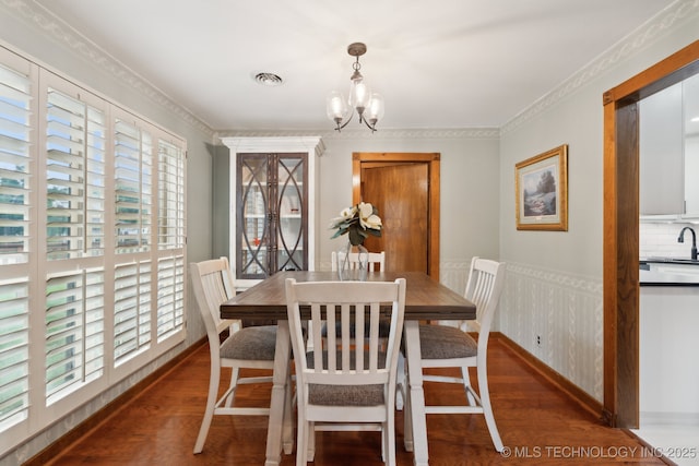 dining space with wood finished floors, plenty of natural light, a chandelier, a wainscoted wall, and crown molding