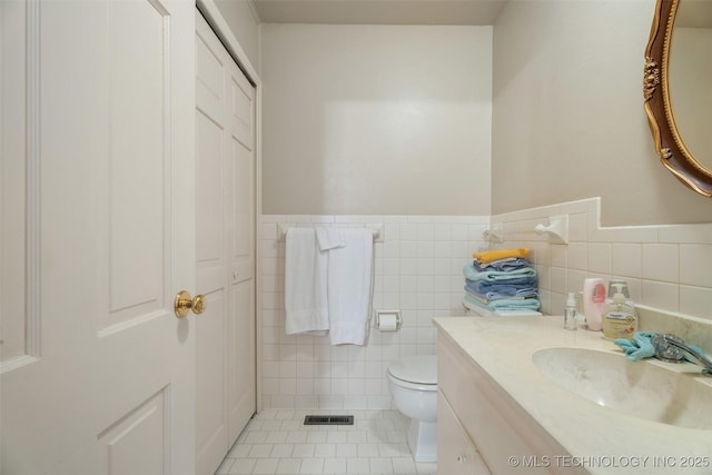 107 W 12th St Unit 107, Bartlesville, OK 74003 - bathroom featuring toilet, tile patterned floors, tile walls, vanity, and wainscoting