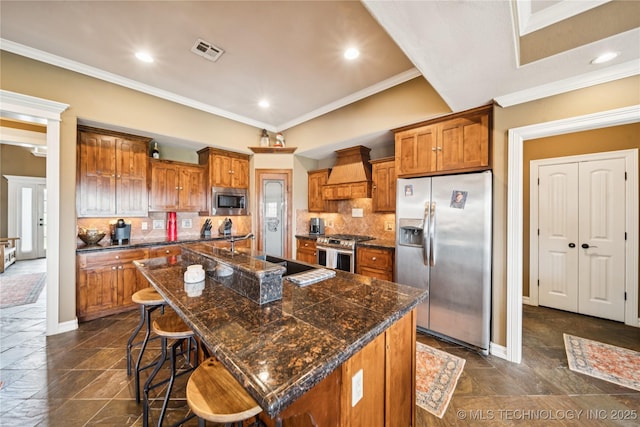 14538 S Urbana Ct, Bixby, OK 74008 - kitchen with appliances with stainless steel finishes, custom exhaust hood, brown cabinetry, a breakfast bar, and an island with sink