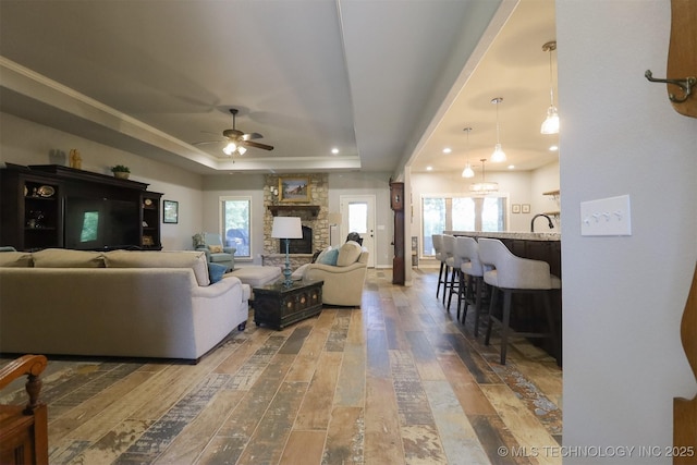 17061 S Creekwood Trl, Claremore, OK 74017 - living area featuring a raised ceiling, wood-type flooring, a ceiling fan, a fireplace, and recessed lighting