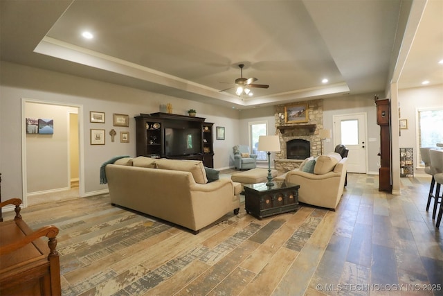 17061 S Creekwood Trl, Claremore, OK 74017 - living room featuring a tray ceiling, ceiling fan, wood-type flooring, a stone fireplace, and baseboards