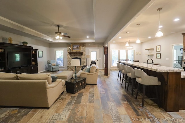 17061 S Creekwood Trl, Claremore, OK 74017 - living area featuring a raised ceiling, dark wood-style floors, a ceiling fan, recessed lighting, and a stone fireplace