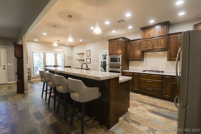 17061 S Creekwood Trl, Claremore, OK 74017 - kitchen featuring stainless steel appliances, dark wood finished floors, recessed lighting, a kitchen island with sink, and decorative backsplash