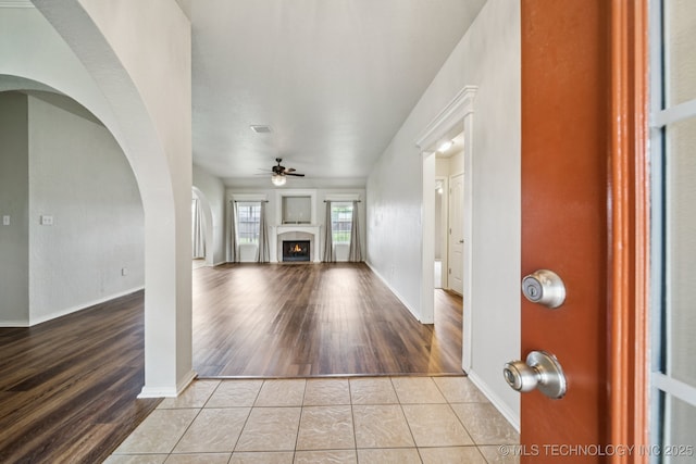 109 W 133rd Pl, Skiatook, OK 74070 - unfurnished living room featuring a ceiling fan, a lit fireplace, wood finished floors, arched walkways, and baseboards