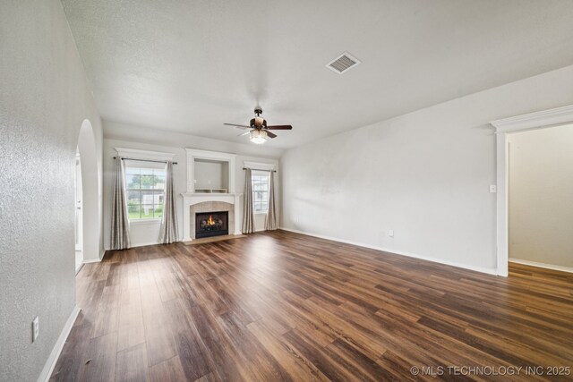 109 W 133rd Pl, Skiatook, OK 74070 - unfurnished living room featuring dark wood-style floors, a ceiling fan, arched walkways, a tile fireplace, and baseboards