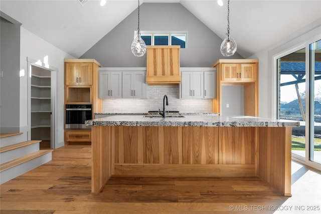 2332 E 135th Dr S, Bixby, OK 74008 - kitchen with oven, a kitchen island with sink, tasteful backsplash, light wood-type flooring, and light stone counters
