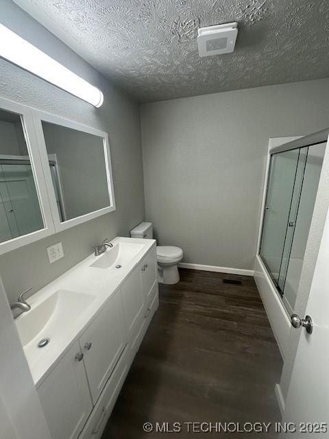 111 E 13th Pl, Claremore, OK 74017 - full bathroom with toilet, wood finished floors, a textured ceiling, double vanity, and baseboards