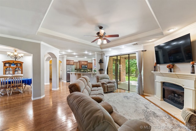 18932 Spring Creek Ln, Claremore, OK 74017 - living area featuring arched walkways, ceiling fan, a tray ceiling, a fireplace with raised hearth, and baseboards