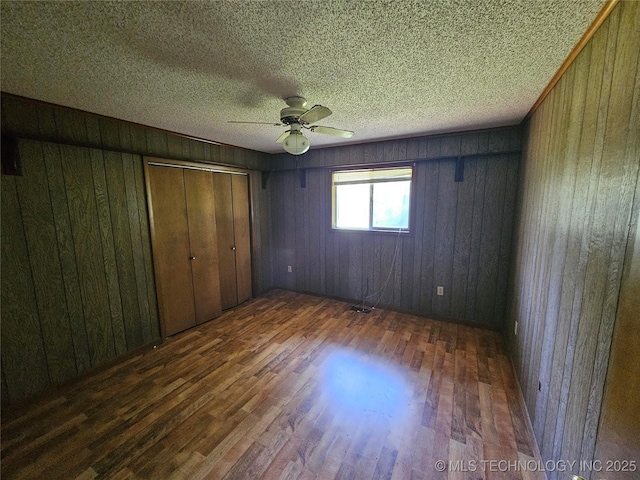 2700 N Witte St, Poteau, OK 74953 - unfurnished bedroom with wood finished floors, wooden walls, a textured ceiling, and a ceiling fan