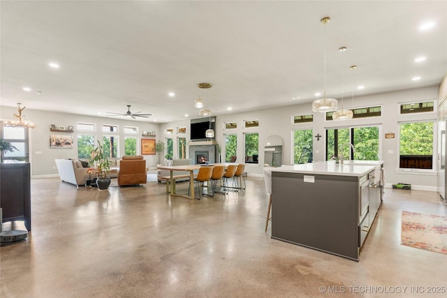 8562 Adams Creek Rd, Beggs, OK 74421 - kitchen with recessed lighting, a warm lit fireplace, an island with sink, decorative light fixtures, and light countertops