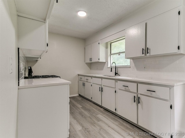 1405 S Cedar St, Bristow, OK 74010 - kitchen featuring light wood-style flooring, decorative backsplash, white cabinetry, a textured ceiling, and light countertops