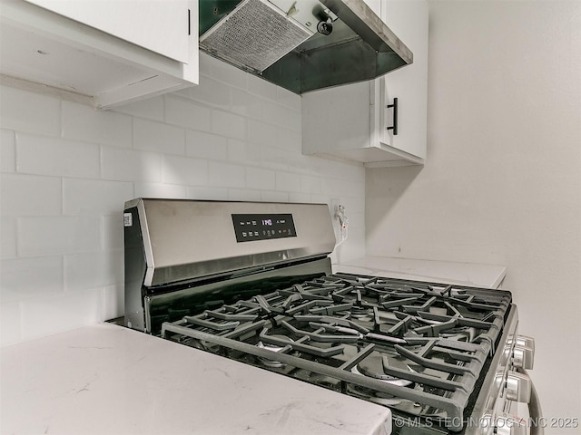 1405 S Cedar St, Bristow, OK 74010 - kitchen view of stainless steel gas range, extractor fan, decorative backsplash, white cabinets, and light stone countertops