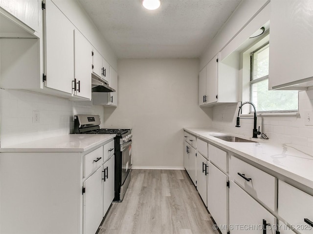 1405 S Cedar St, Bristow, OK 74010 - kitchen featuring stainless steel gas range, under cabinet range hood, white cabinets, light wood finished floors, and tasteful backsplash