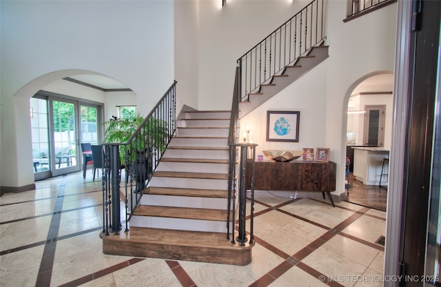 3704 River Bend Rd, Muskogee, OK 74403 - stairs with inlaid floor details, a towering ceiling, arched walkways, baseboards, and crown molding
