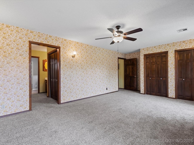 639 Oakridge Dr, Bartlesville, OK 74006 - unfurnished bedroom featuring carpet, two closets, a textured ceiling, wallpapered walls, and ceiling fan