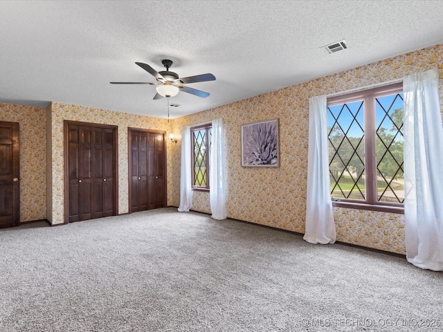639 Oakridge Dr, Bartlesville, OK 74006 - unfurnished bedroom with wallpapered walls, a textured ceiling, multiple closets, carpet floors, and a ceiling fan