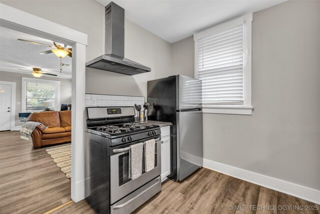 149 N Columbia Pl, Tulsa, OK 74110 - kitchen featuring appliances with stainless steel finishes, wall chimney exhaust hood, a ceiling fan, light wood-type flooring, and decorative backsplash