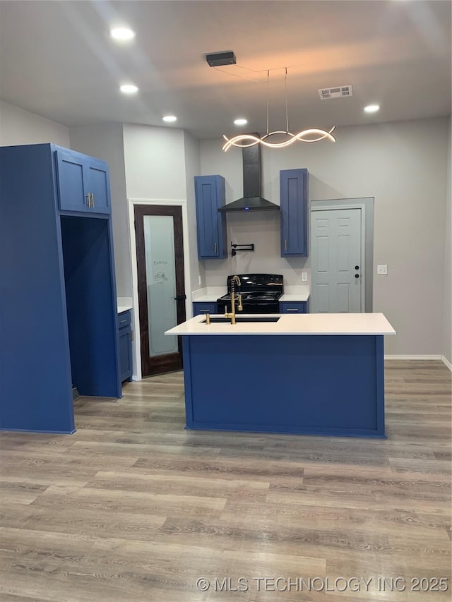 509 S Harrison St, Cushing, OK 74023 - kitchen featuring wall chimney exhaust hood, blue cabinets, light countertops, a center island with sink, and recessed lighting