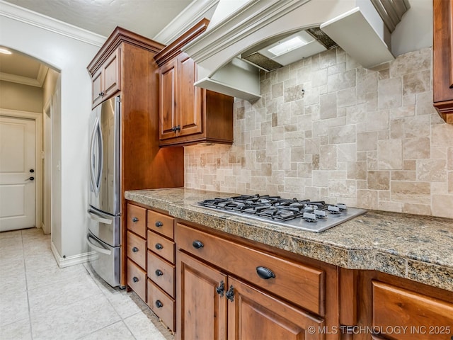9025 N 100th E Ave, Owasso, OK 74055 - kitchen with appliances with stainless steel finishes, arched walkways, brown cabinetry, custom range hood, and decorative backsplash