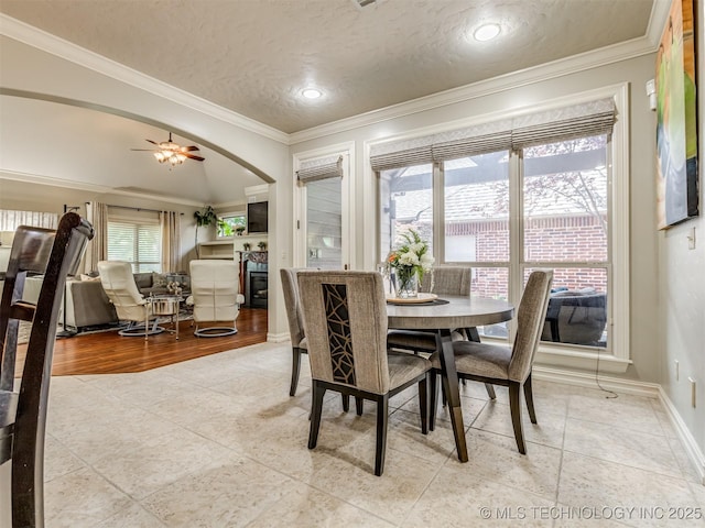 9025 N 100th E Ave, Owasso, OK 74055 - dining space with ornamental molding, arched walkways, light tile patterned flooring, a glass covered fireplace, and ceiling fan