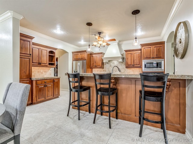 9025 N 100th E Ave, Owasso, OK 74055 - kitchen featuring stainless steel appliances, arched walkways, custom range hood, brown cabinetry, and decorative backsplash