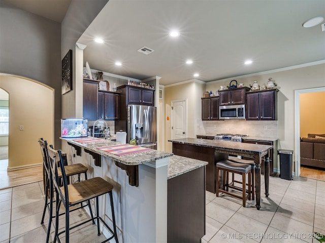 2610 E 139th St S, Bixby, OK 74008 - kitchen with stainless steel appliances, a breakfast bar, arched walkways, light tile patterned flooring, and recessed lighting