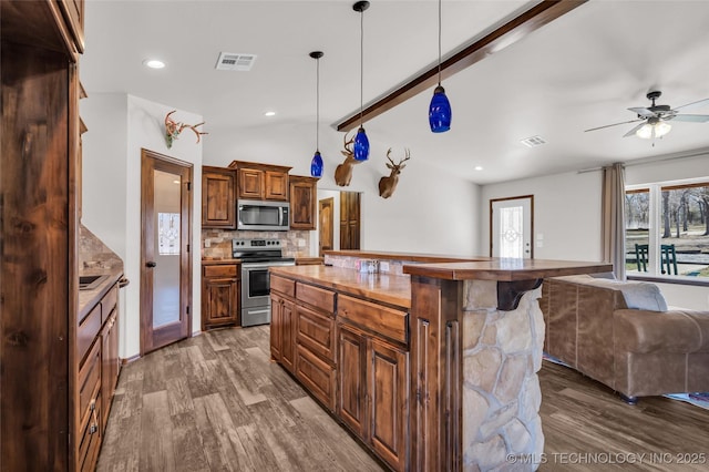 6335 S Watson, Sulphur, OK 73086 - kitchen featuring appliances with stainless steel finishes, open floor plan, wood finished floors, a breakfast bar area, and tasteful backsplash