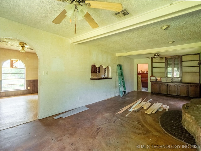 1015 Diehl Ln, Hartshorne, OK 74547 - unfurnished living room with a ceiling fan, a textured ceiling, unfinished concrete floors, arched walkways, and a wainscoted wall