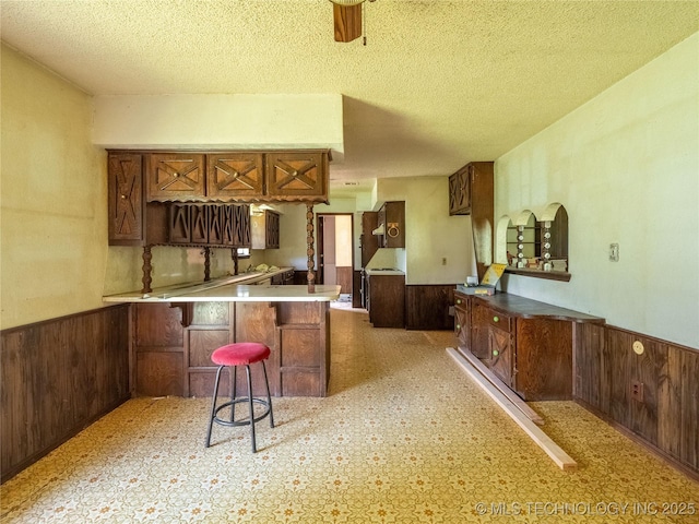 1015 Diehl Ln, Hartshorne, OK 74547 - kitchen featuring wainscoting, a peninsula, a textured ceiling, a breakfast bar, and wooden walls