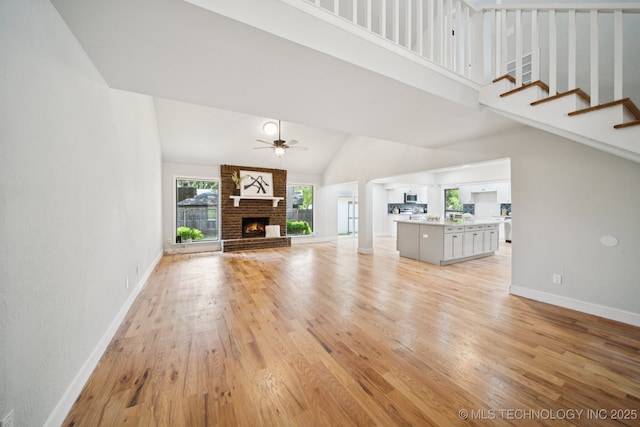 7927 S 86th E Ave, Tulsa, OK 74133 - unfurnished living room with high vaulted ceiling, light wood-type flooring, a ceiling fan, a fireplace, and stairs