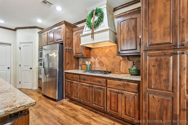 4733 S 167th E Pl, Tulsa, OK 74134 - kitchen featuring stainless steel appliances, crown molding, backsplash, light wood-type flooring, and custom range hood