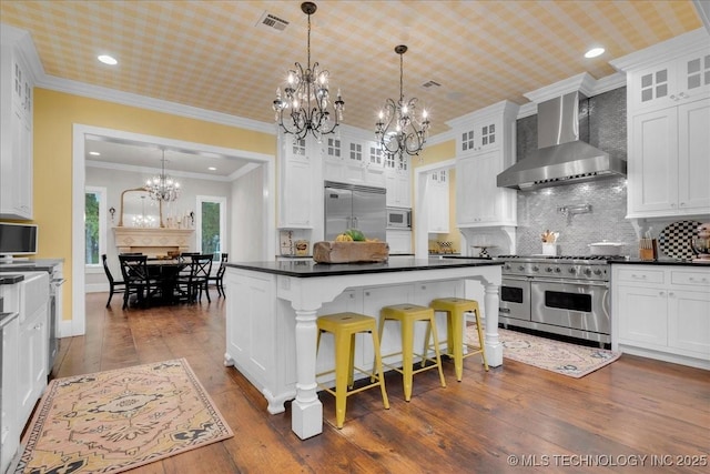 20565 E Clear Brook Rd, Owasso, OK 74055 - kitchen with wall chimney range hood, built in appliances, a chandelier, dark countertops, and white cabinetry