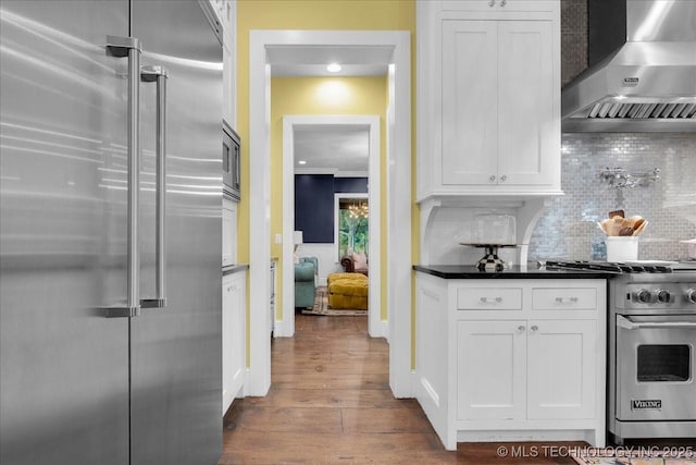 20565 E Clear Brook Rd, Owasso, OK 74055 - kitchen with premium appliances, wall chimney exhaust hood, dark countertops, white cabinetry, and wood finished floors