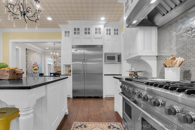 20565 E Clear Brook Rd, Owasso, OK 74055 - kitchen featuring built in appliances, a chandelier, wall chimney exhaust hood, dark countertops, and crown molding